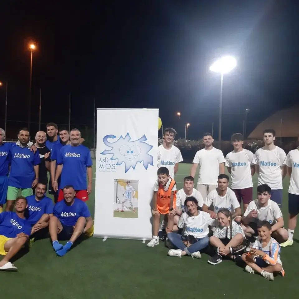Squadre e ragazzi riuniti in campo di sera accanto allo stendardo dell’ASD M.O.S.